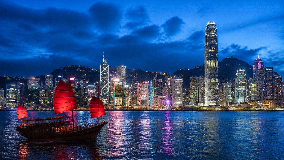 Skyline de Hong Kong sobre la bahía Victoria al anochecer con un barco tradicional Skyline de Hong Kong sobre la bahía Victoria al anochecer con un barco tradicional